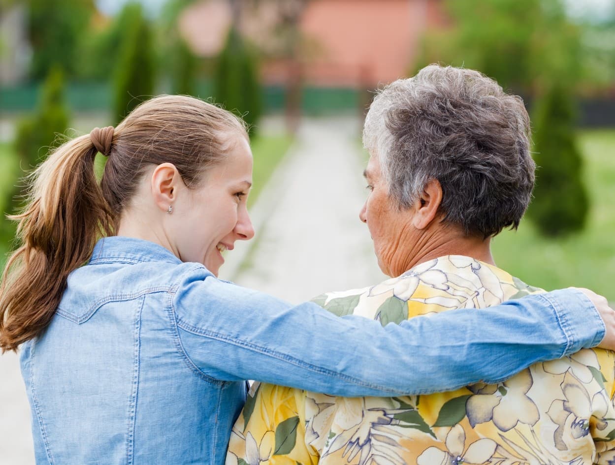 A young woman walks beside an older woman with an arm around her shoulders.