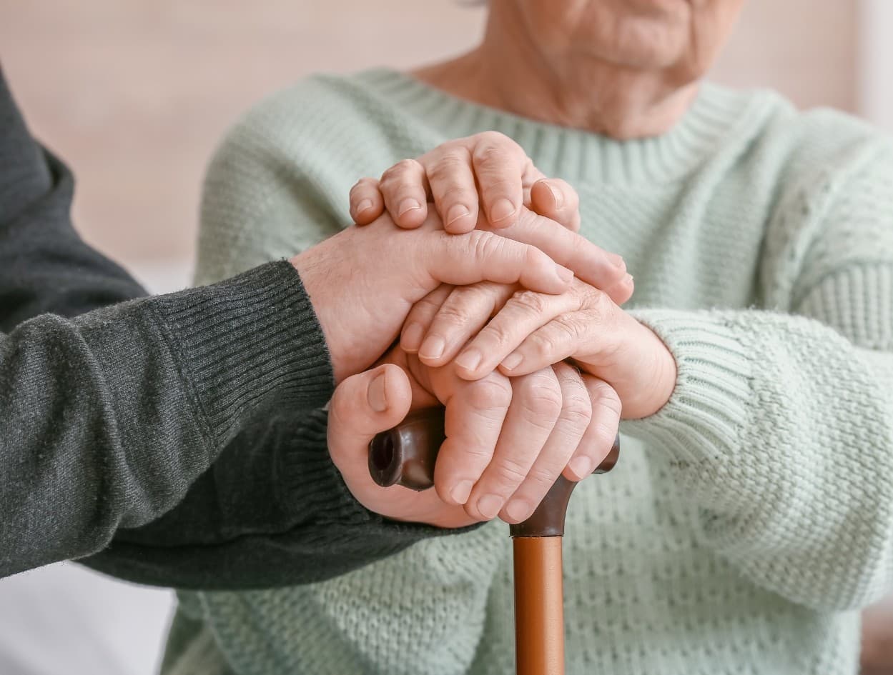 Hands resting together on an older person’s walking cane.