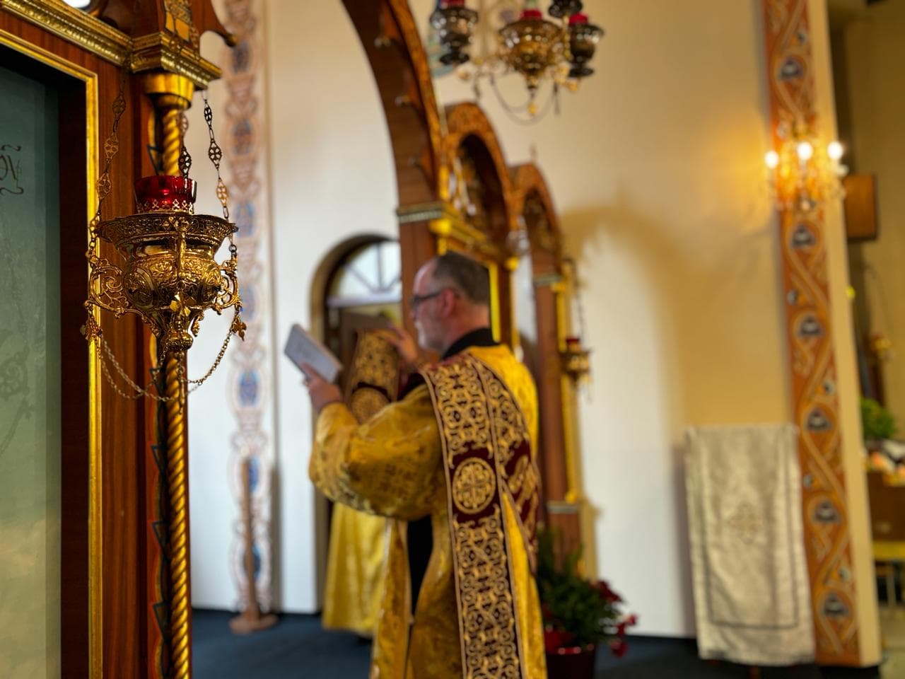 A man in ornate liturgical vestments reading during a church service.