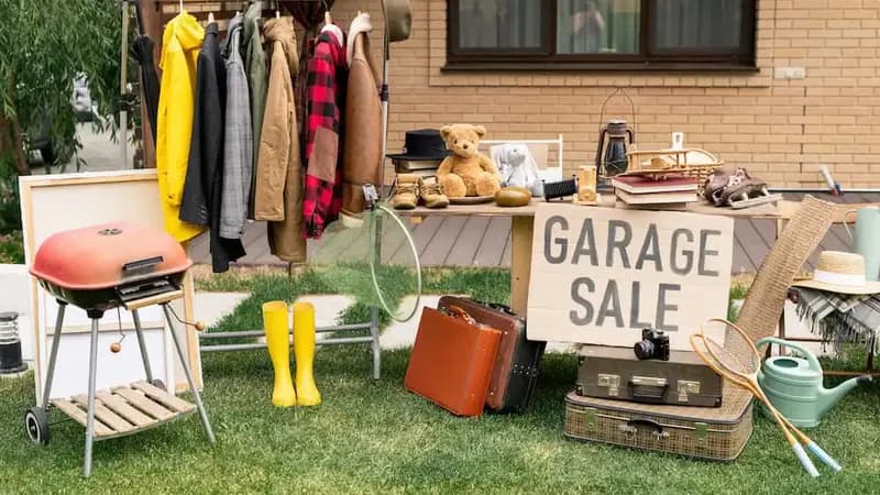 Garage sale with clothes, toys, books, and household items displayed on racks and tables.