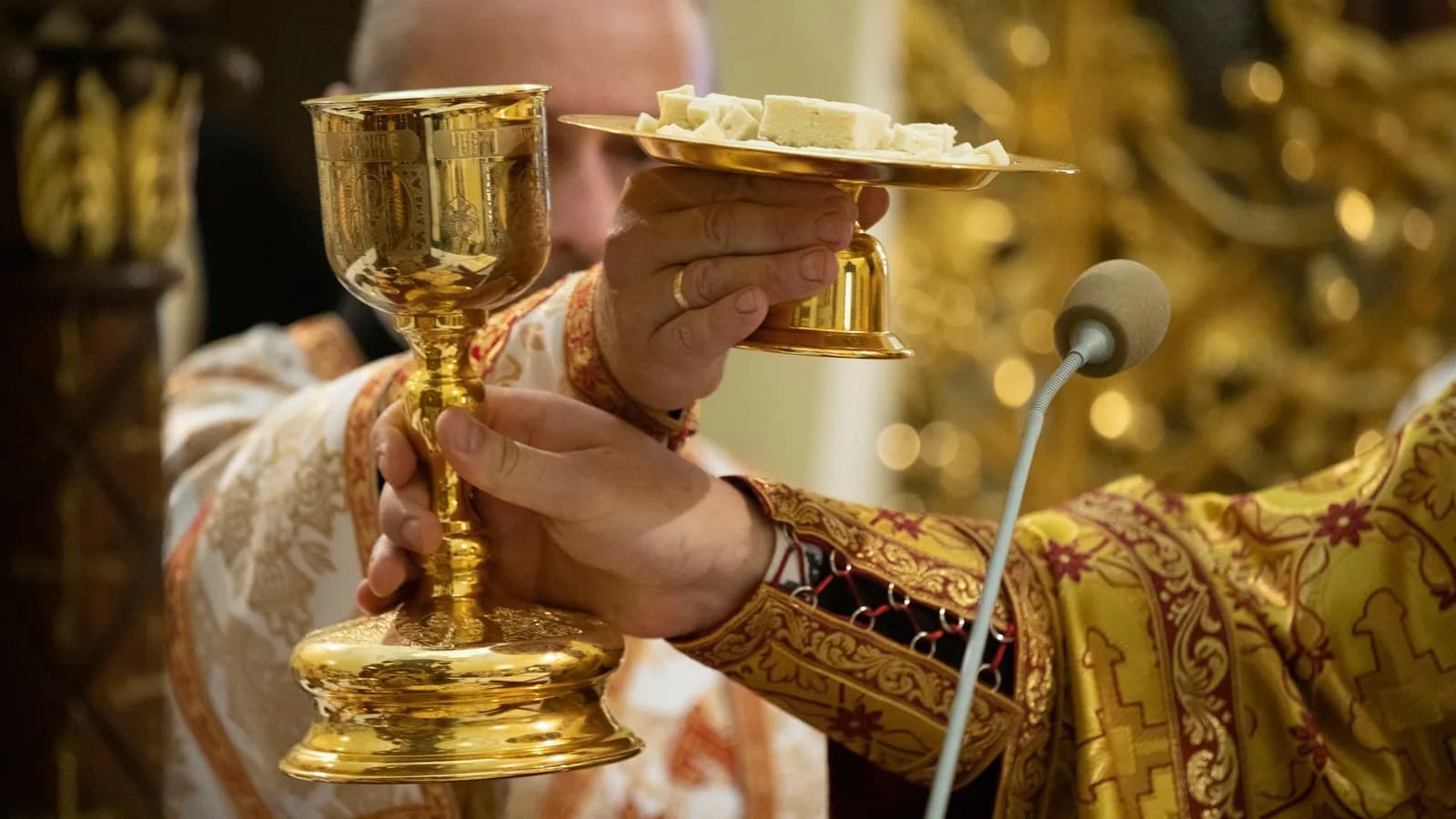 Priest holds golden chalice and paten with prosphora during Divine Liturgy.