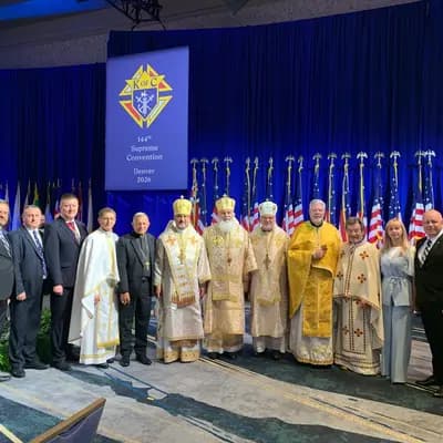 Clergy in liturgical vestments and laymen stand before a K of C banner
